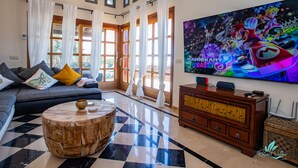Un salon avec un canapé, une table basse, un téléviseur et une grande fenêtre avec des rideaux.