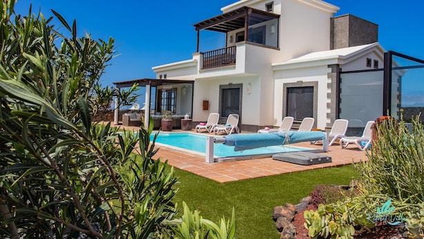 Une maison moderne à deux étages dotée d’une piscine, d’un espace extérieur aménagé et d’un jardin luxuriant.