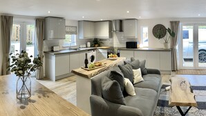 Une cuisine moderne avec des meubles gris, un îlot central et un coin repas comprenant un canapé gris et une table basse.