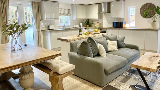Une cuisine moderne avec des meubles blancs, un îlot central en bois et un canapé gris.