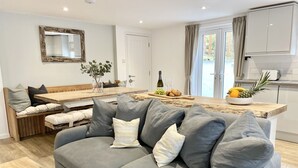 Un salon moderne avec un canapé gris, un banc en bois et un coin repas doté d’une table en bois.