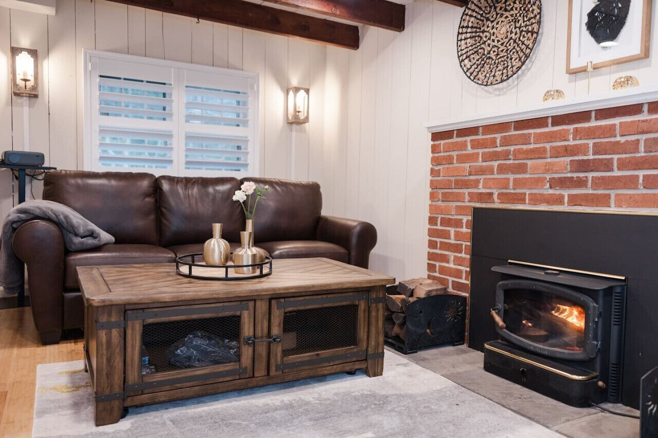 Una sala de estar acogedora con un sofá de cuero, una mesa de centro de madera con objetos decorativos, una chimenea y una pared de ladrillo.