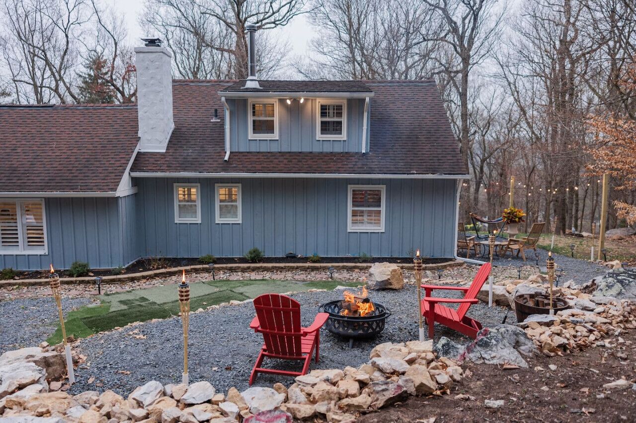 A house with a grey exterior, a chimney, and a deck area with red chairs and a fire pit.