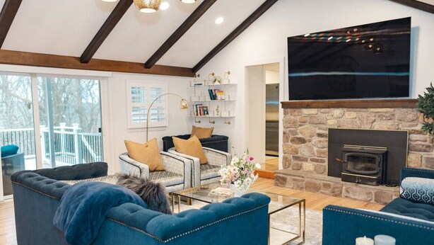 A modern living room with a stone fireplace, a large TV mounted on the wall, and a balcony with a railing. - Superior Guest Room w Hot Tub w Outdoor view (New Hope)