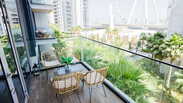 A balcony with wicker furniture, a glass table, and a view of a cityscape with palm trees. - Aya - Stunning 1BR Surrounding The Sea Views & Ain Dubai (Dubai)