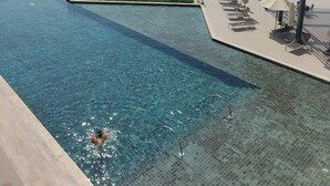 A clear blue infinity pool with a view of the sea, a covered seating area with umbrellas, and a palm tree. - Aya - Stunning 1BR Surrounding The Sea Views & Ain Dubai (Dubai)