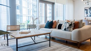 A modern living room with a sofa, coffee table, and chairs. There is a dining area with a table and chairs. Large windows provide natural light and views of the city. - Aya - Stunning 1BR Surrounding The Sea Views & Ain Dubai (Dubai)
