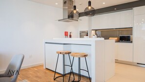 A modern kitchen with white cabinetry, a central island with stools, and pendant lighting. - Aya - Stunning 1BR Surrounding The Sea Views & Ain Dubai (Dubai)