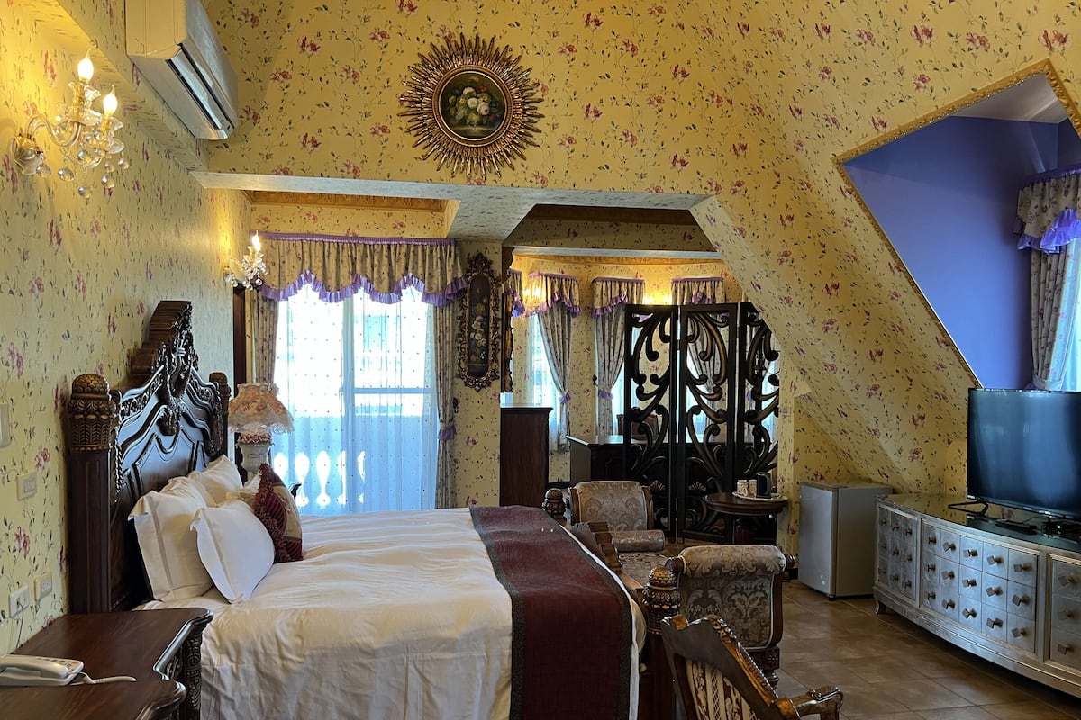 A bedroom with a large bed, a dresser, a television, and a decorative mirror.