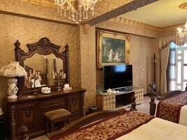 A luxurious bedroom with a large bed, a wooden dresser, a television, and a chandelier.