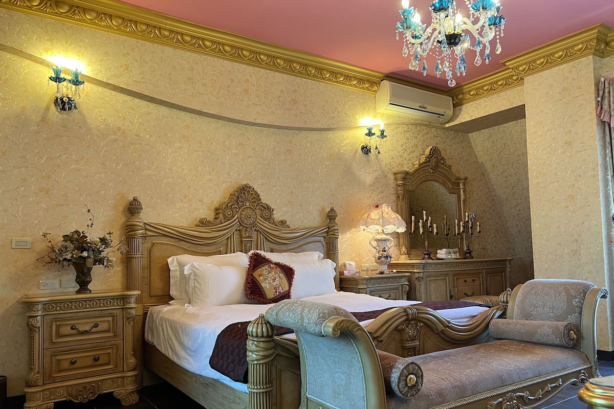 A luxurious bedroom with a large bed, ornate headboard, and a chandelier.