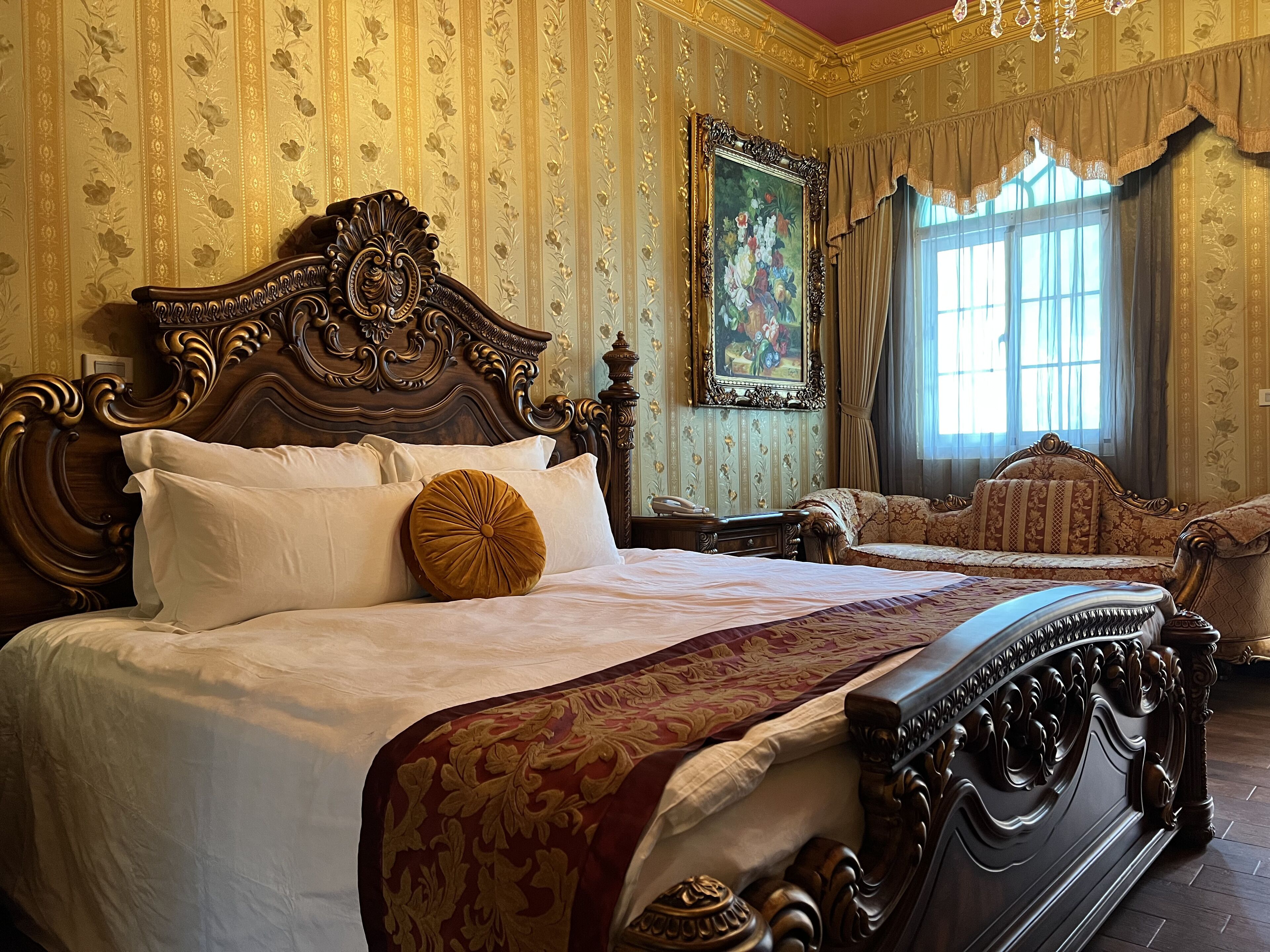 A classic, ornately decorated bedroom with a large bed, a sofa, and a painting on the wall.