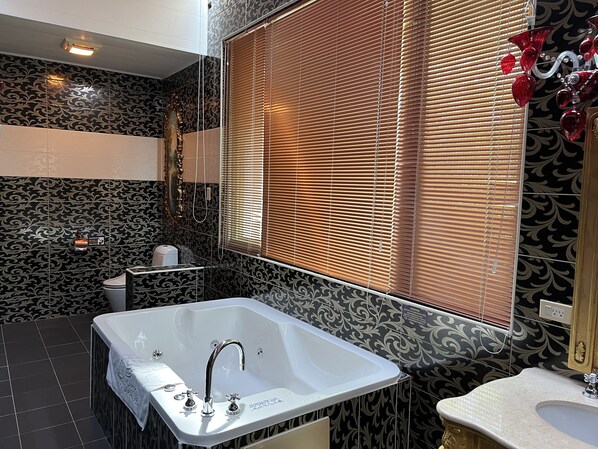 A bathroom with a large bathtub, a toilet, and a sink. There is a window with blinds and a decorative glass piece on the window sill. - olliere castle (Puli)
