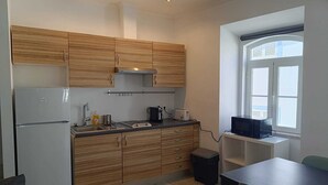 A compact kitchen with wooden cabinets, a built-in oven, and a window with blinds. - Beach Haven (Albufeira)