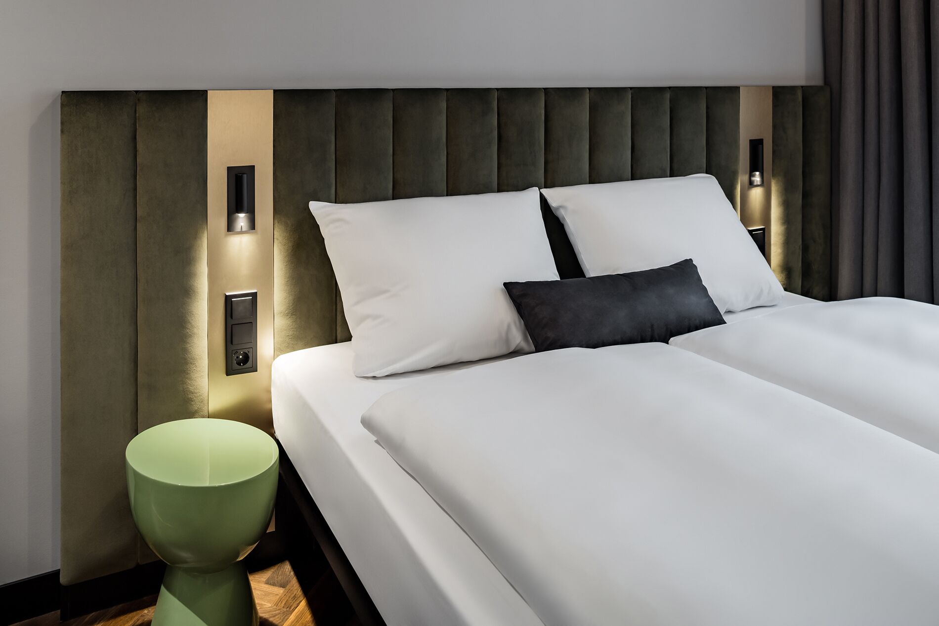 Une chambre d’hôtel moderne avec un grand lit, une table de chevet verte et des lampes fixées au mur.