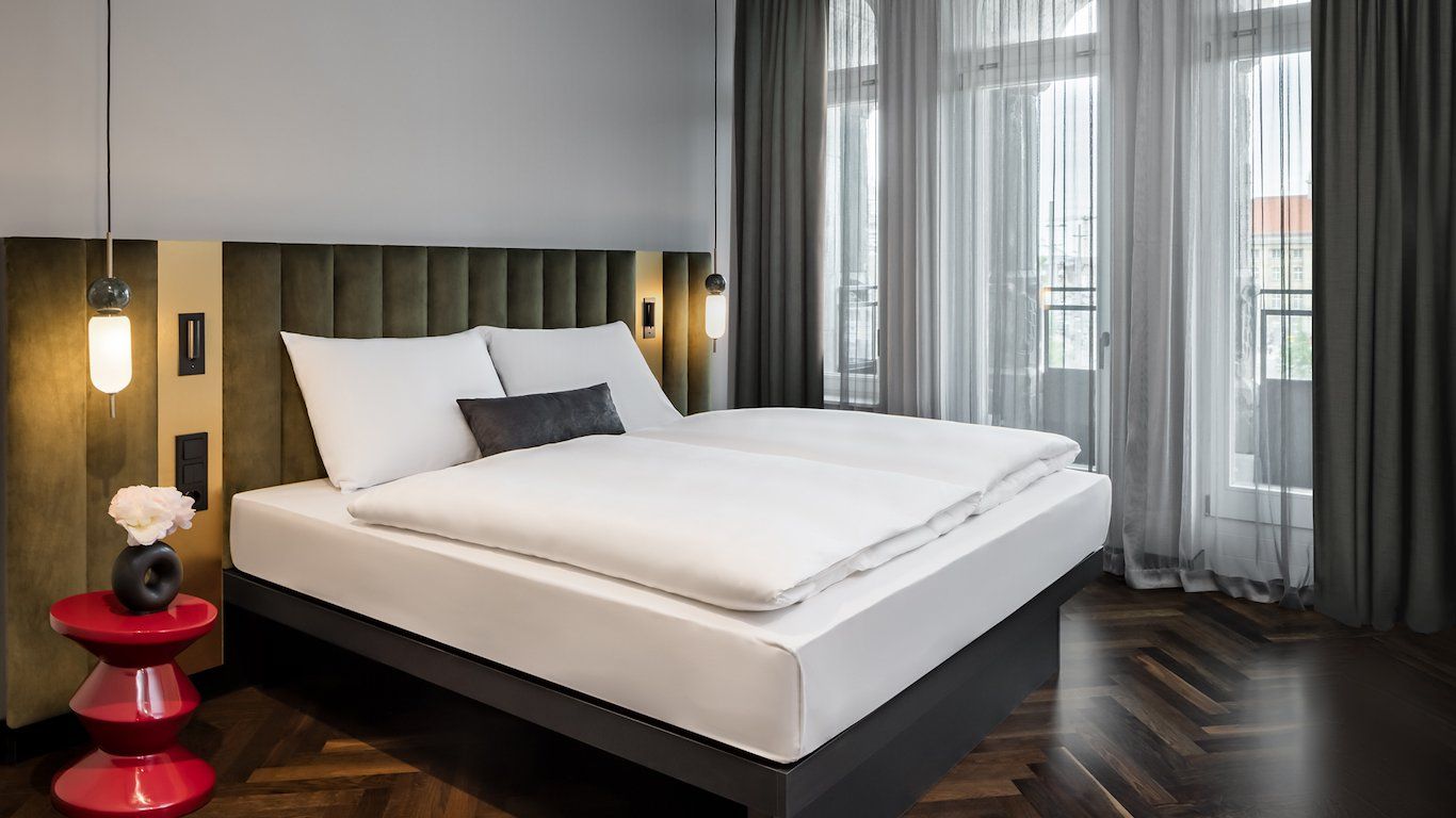 Une chambre d’hôtel moderne avec un grand lit, une table de chevet rouge et un luminaire fixé au mur.