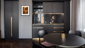 A modern kitchen with dark cabinetry, a marble countertop, and a round dining table with chairs. - AMANO Home Leipzig (Leipzig)