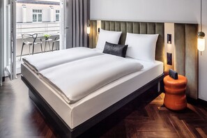 A modern hotel room with a large bed, a wooden floor, and a balcony with chairs and a table. - AMANO Home Leipzig (Leipzig)