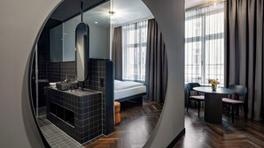 Una camera d'hotel moderna con uno specchio circolare, un letto grande, un bagno con vasca e una zona pranzo con tavolo e sedie.