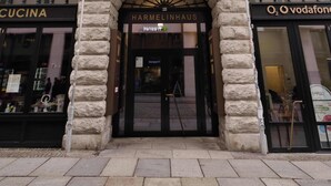 Un edificio in pietra con le insegne 'AMANO HOME' e 'HARMELINHAUS', caratterizzato da finestre ad arco e un ingresso centrale.