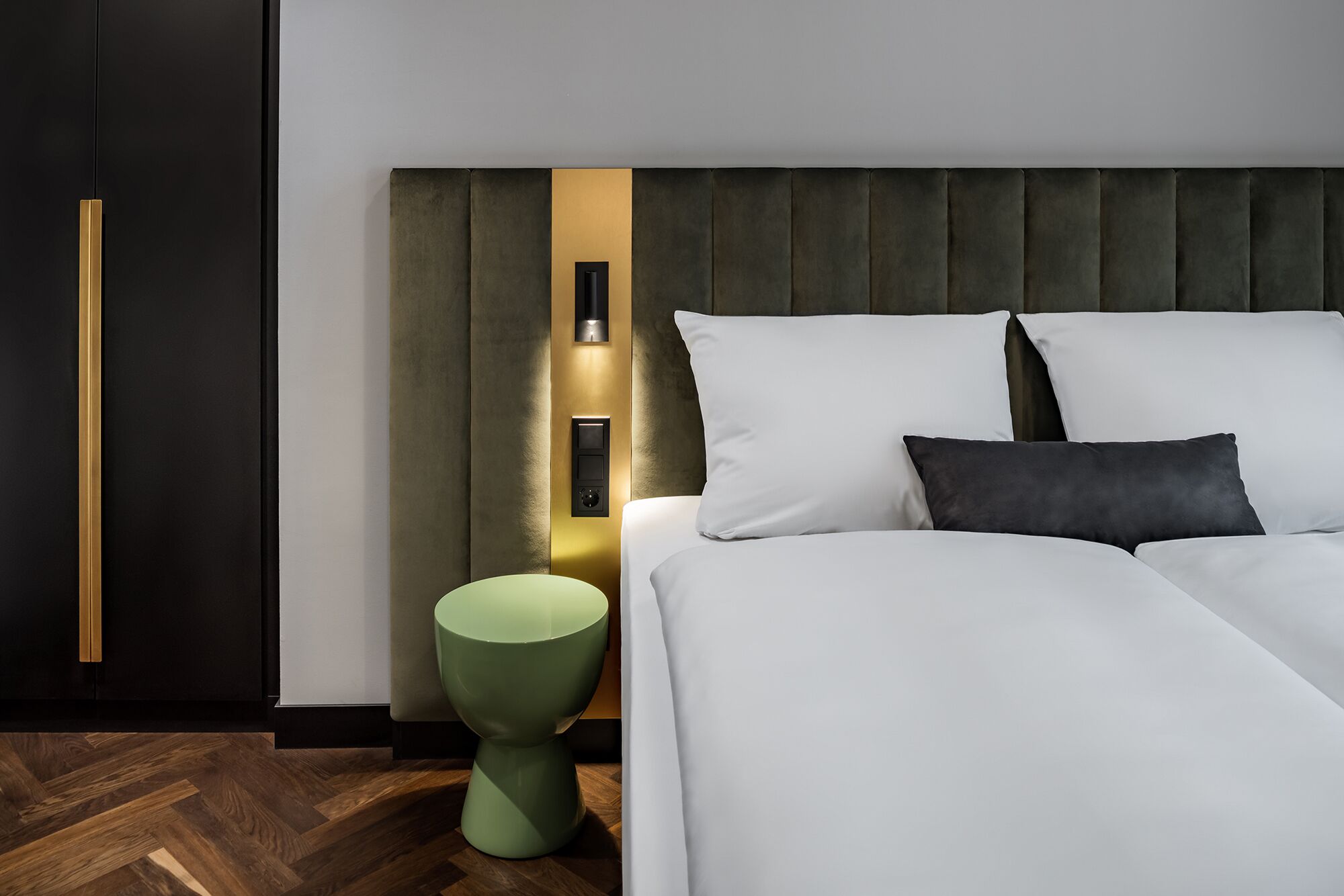 Un dormitorio moderno con una cama grande, un taburete verde decorativo e iluminación empotrada en la pared.