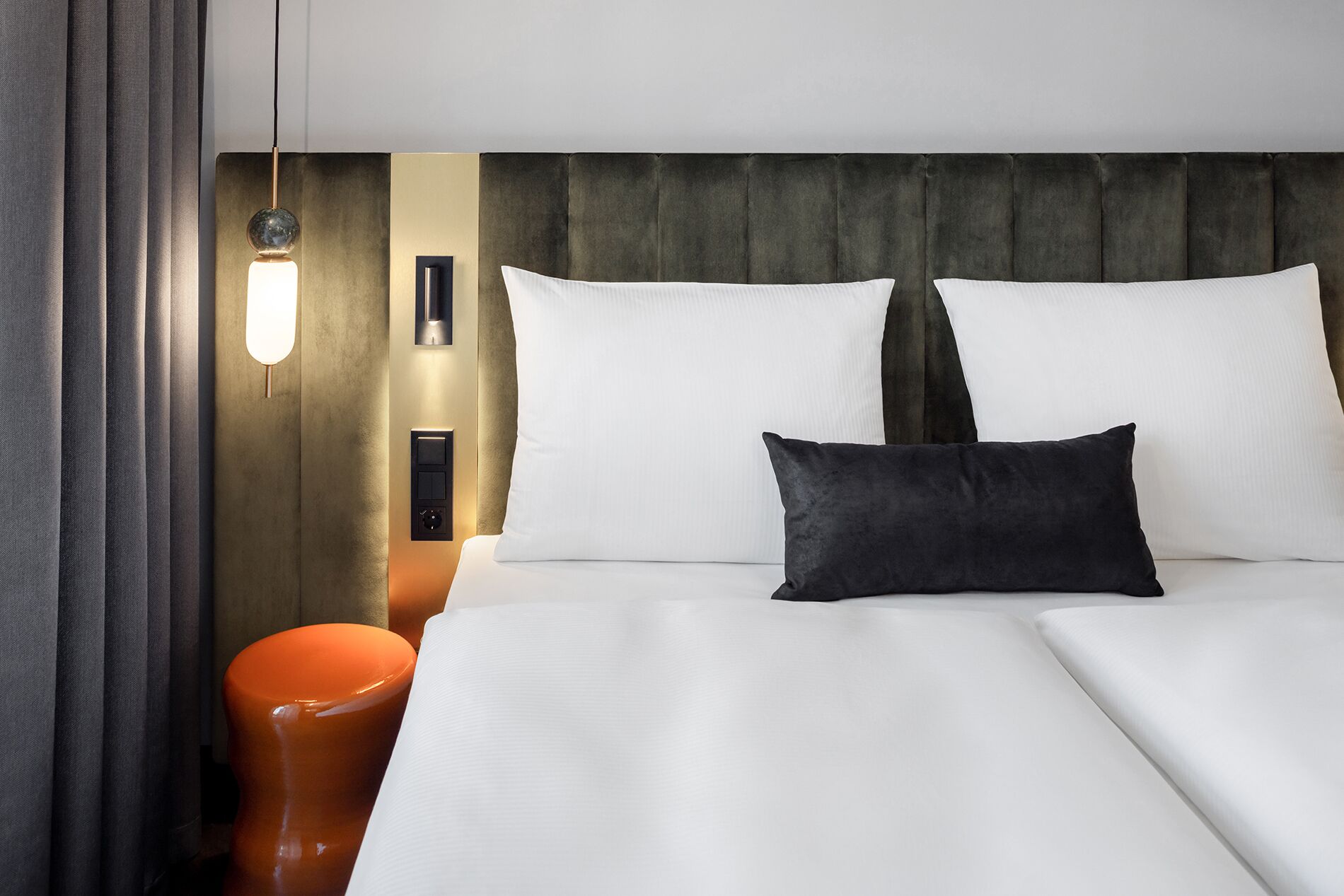 A hotel room with a bed, a nightstand, a lamp, and a wall-mounted control panel.