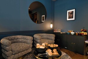 A room with two armchairs, a round mirror, a cabinet with food items, and a framed picture on the wall. - AMANO Home Leipzig (Leipzig)