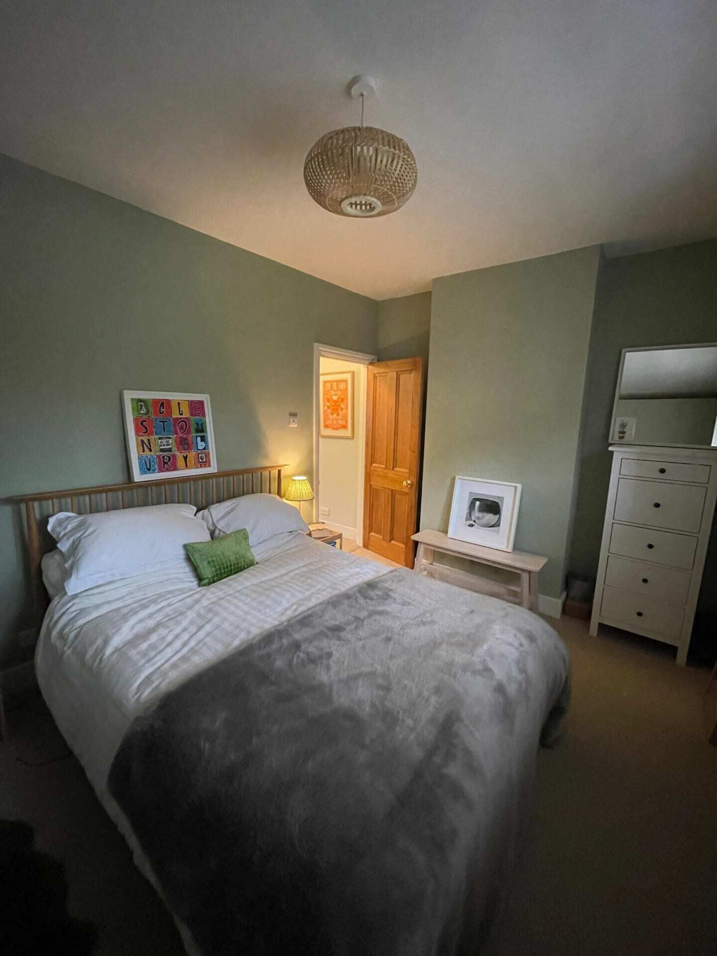 A bedroom with a bed, bedside table, lamp, wardrobe, and a framed picture on the wall.