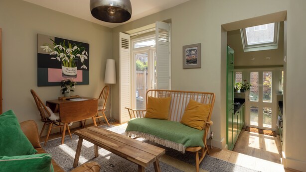 Un salon confortable avec un canapé, une table basse en bois et une table à manger. Une fenêtre offre une vue sur l’extérieur.