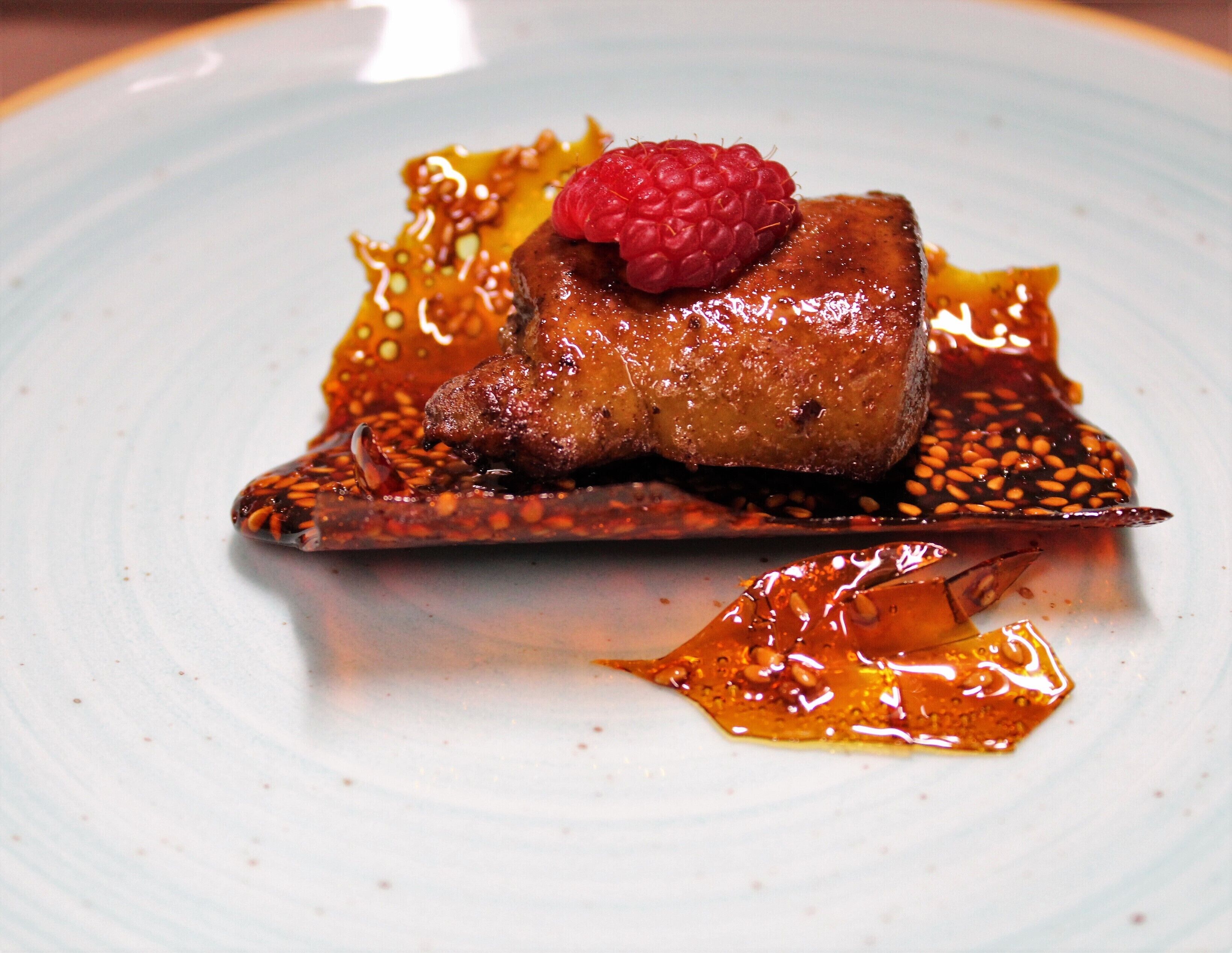 Un postre con una frambuesa encima, servido en un plato con salsa y semillas.