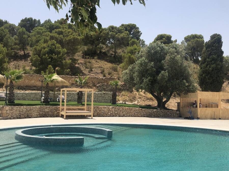 Una piscina con un muro de piedra, un pabellón de madera y una pequeña construcción de madera.