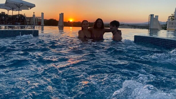 Una piscina al atardecer con tres personas nadando.