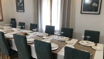 Une salle à manger avec une longue table dressée pour un repas, entourée de chaises, et des œuvres d’art encadrées accrochées aux murs.