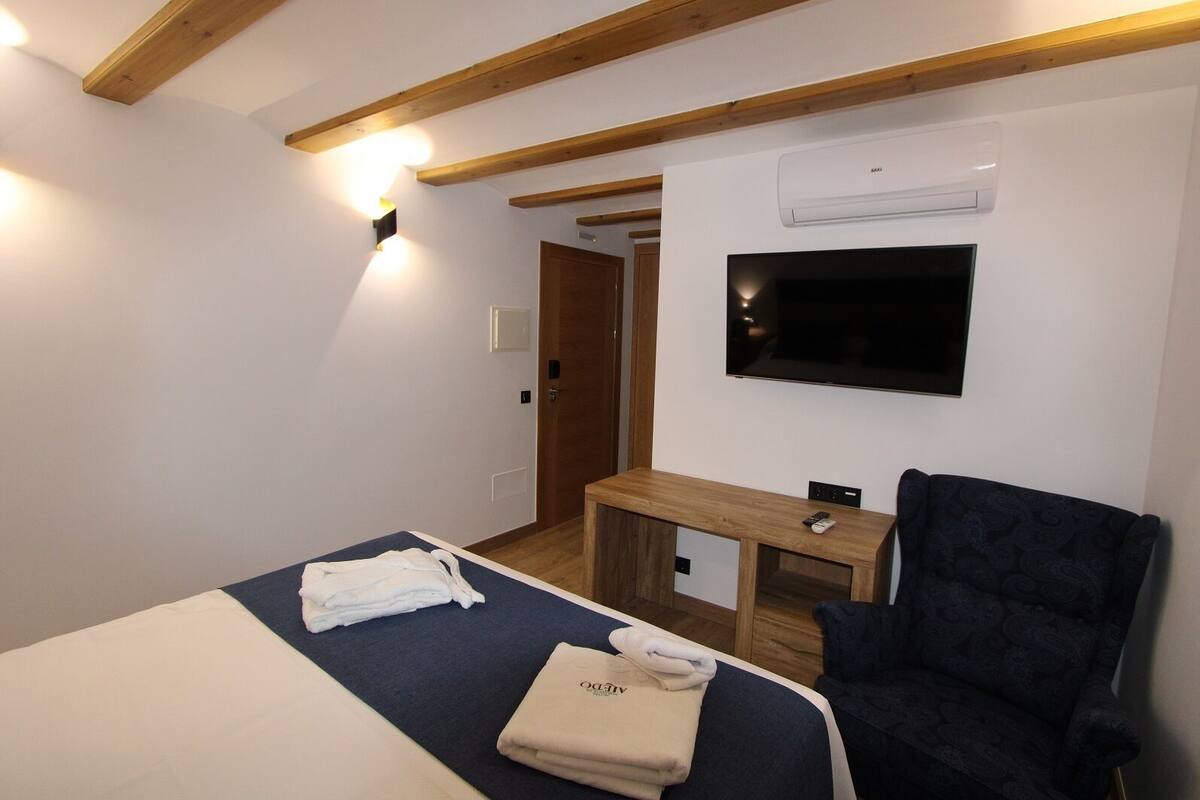 A hotel room with a bed, a desk, a chair, a TV, and an air conditioning unit.