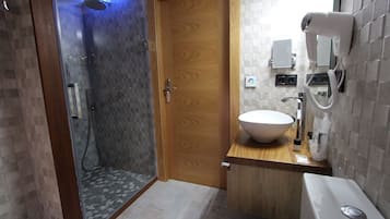Un baño moderno con ducha acristalada, puerta de madera, lavamanos blanco y secador de pelo montado en la pared.