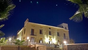 Un edificio de dos pisos con balcón, paredes de piedra y palmeras.
