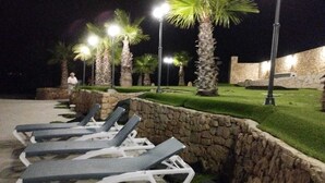 Espacio al aire libre iluminado con lámparas de calle, con sillones de descanso y palmeras.