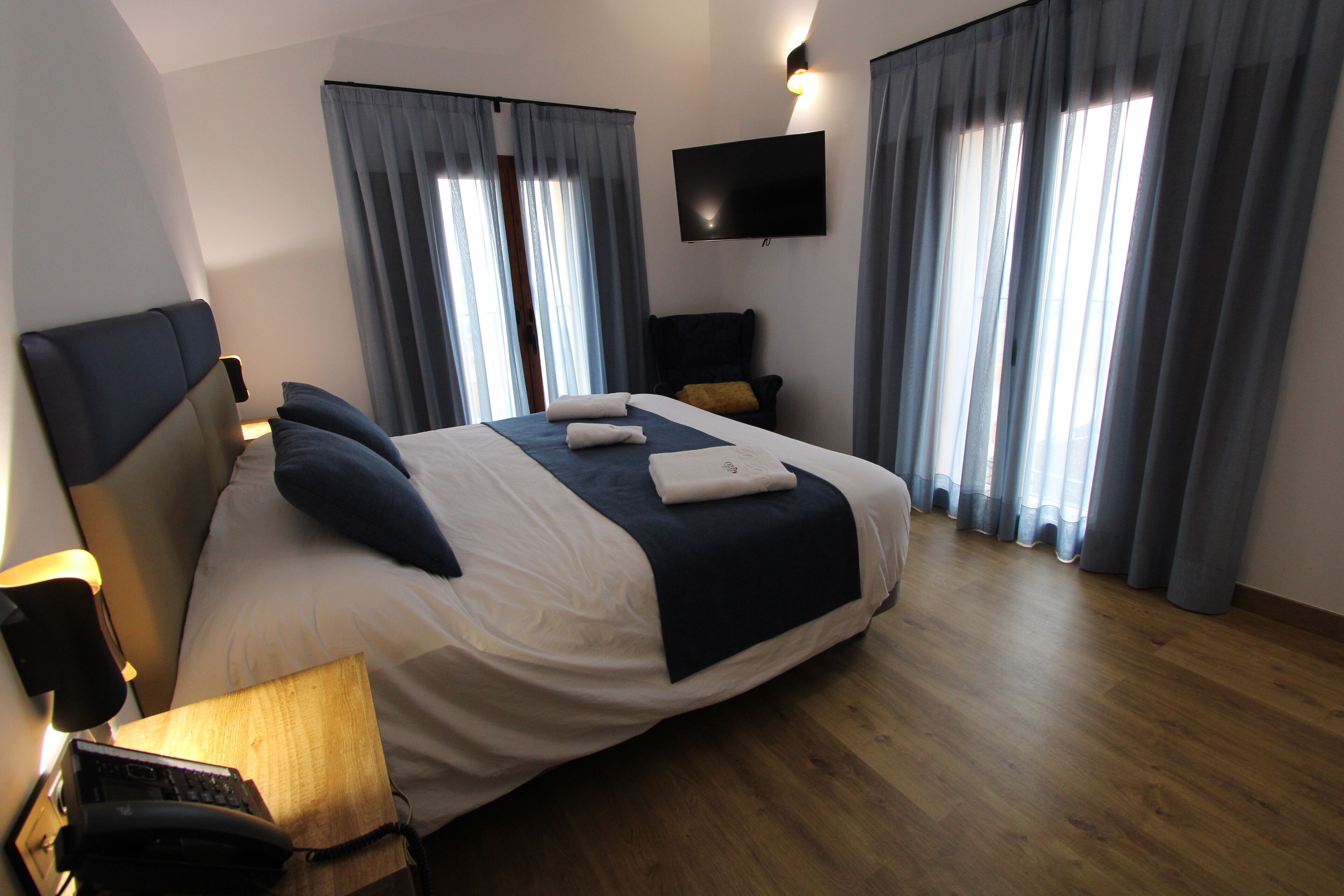 A hotel room with a large bed, a flat-screen TV mounted on the wall, and a wooden floor.