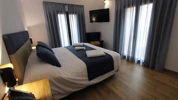 A hotel room with a large bed, a flat-screen TV mounted on the wall, and a wooden floor.