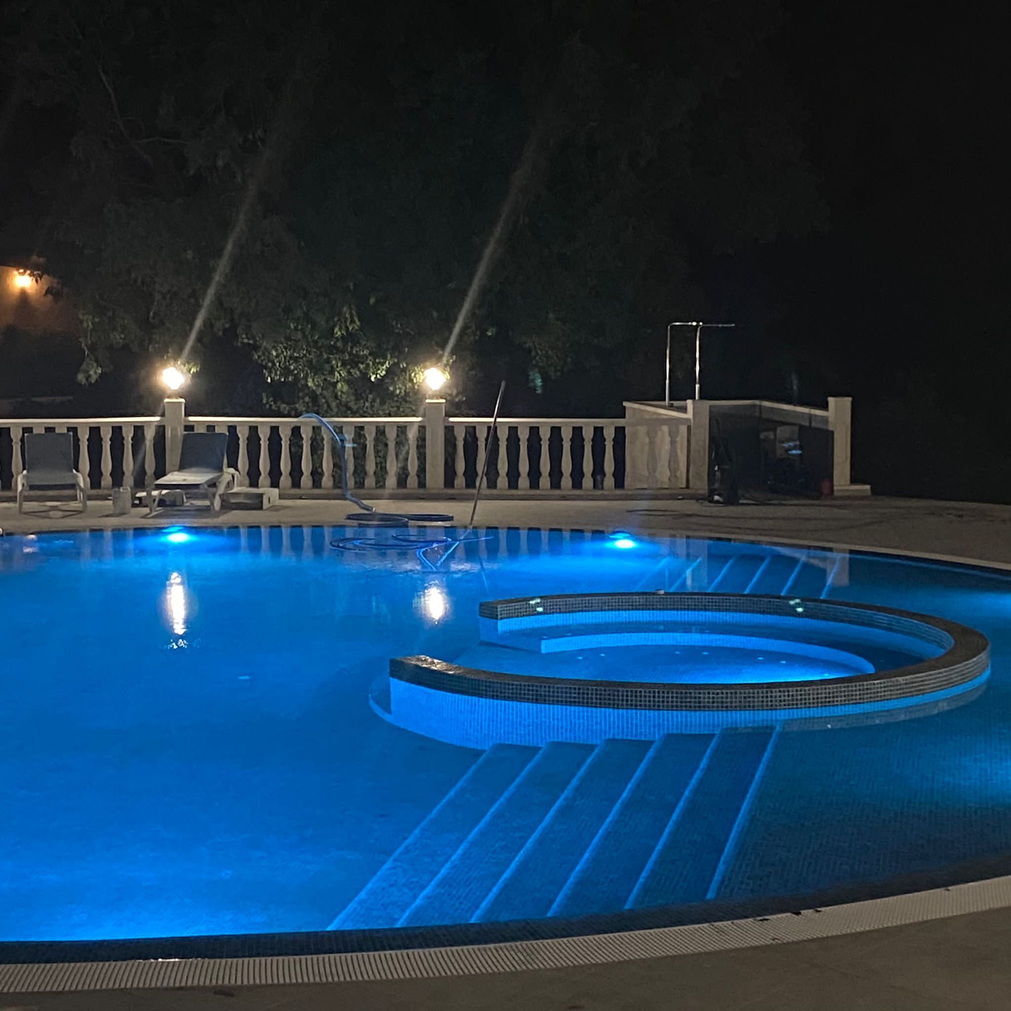 A swimming pool with a circular design, surrounded by a white balustrade and lounge chairs.