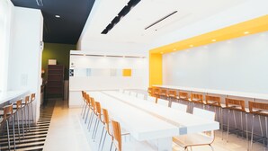A modern dining area with long white tables and wooden chairs.