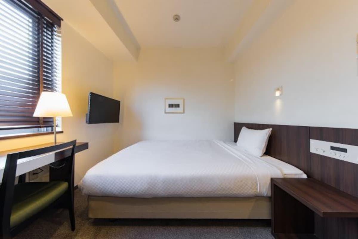 Habitación de hotel con cama, escritorio, silla, televisor y mesita de noche.