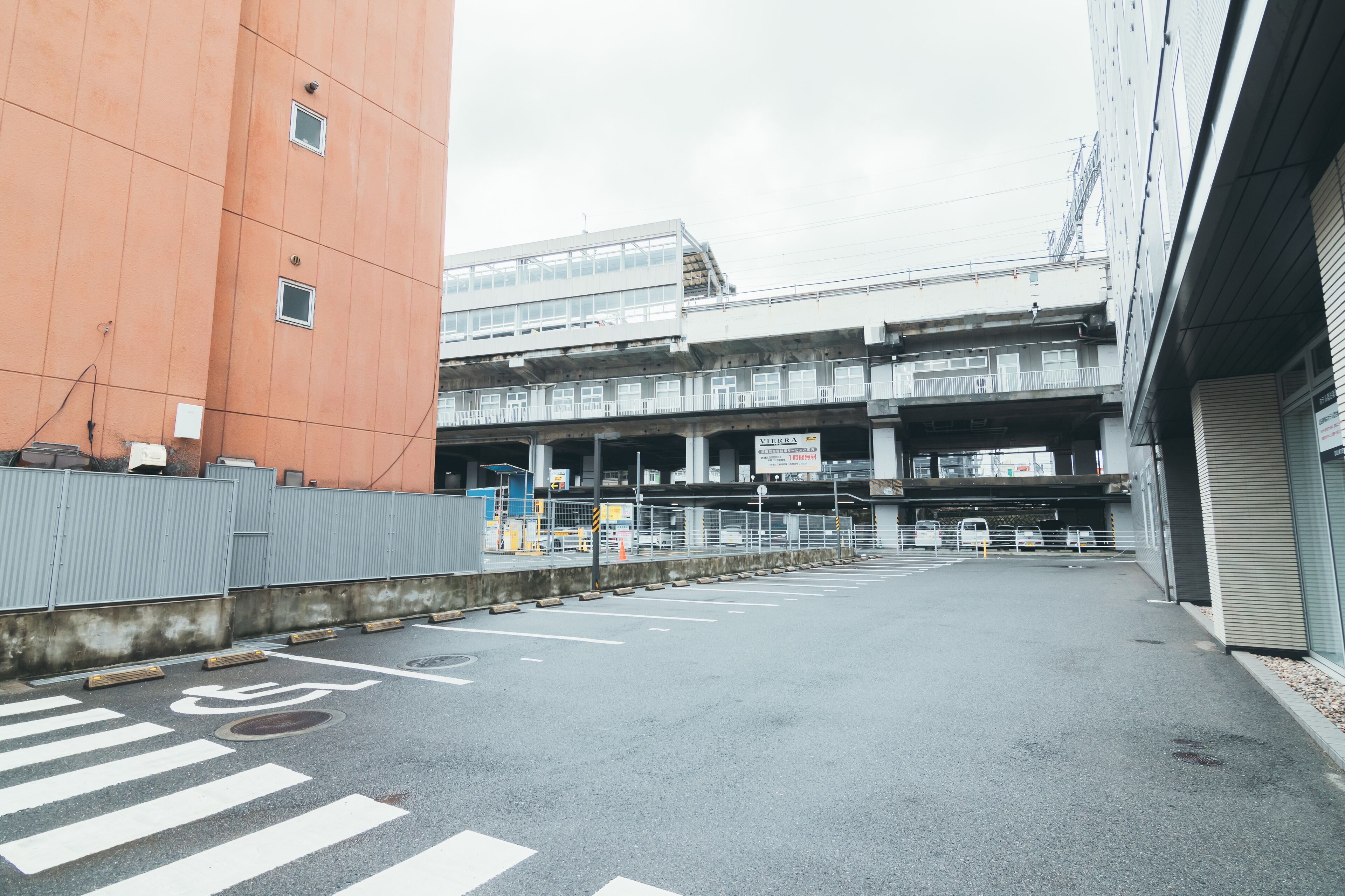 A parking lot with a pedestrian crossing and a multi-story building in the background.
