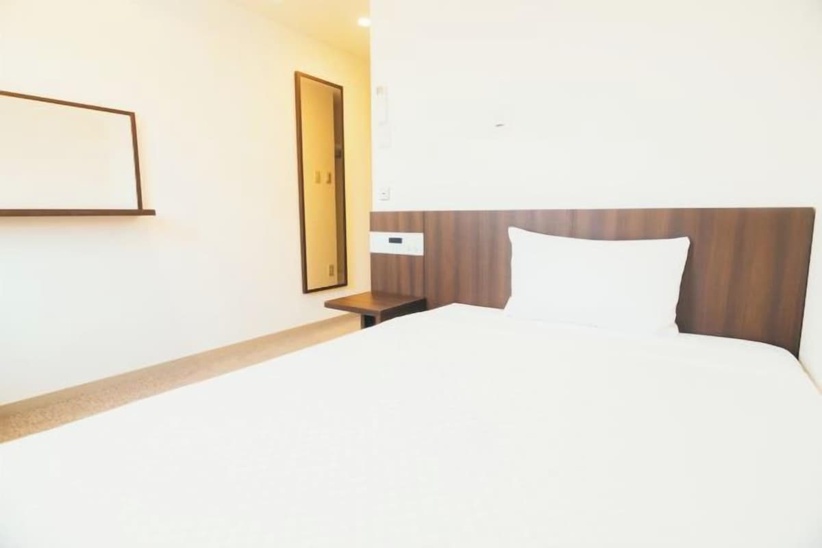 Habitación de hotel con cama, mesita de noche, espejo y lámpara de pared.