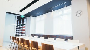 A conference room with a long table, chairs, a bookshelf, and a clock on the wall.