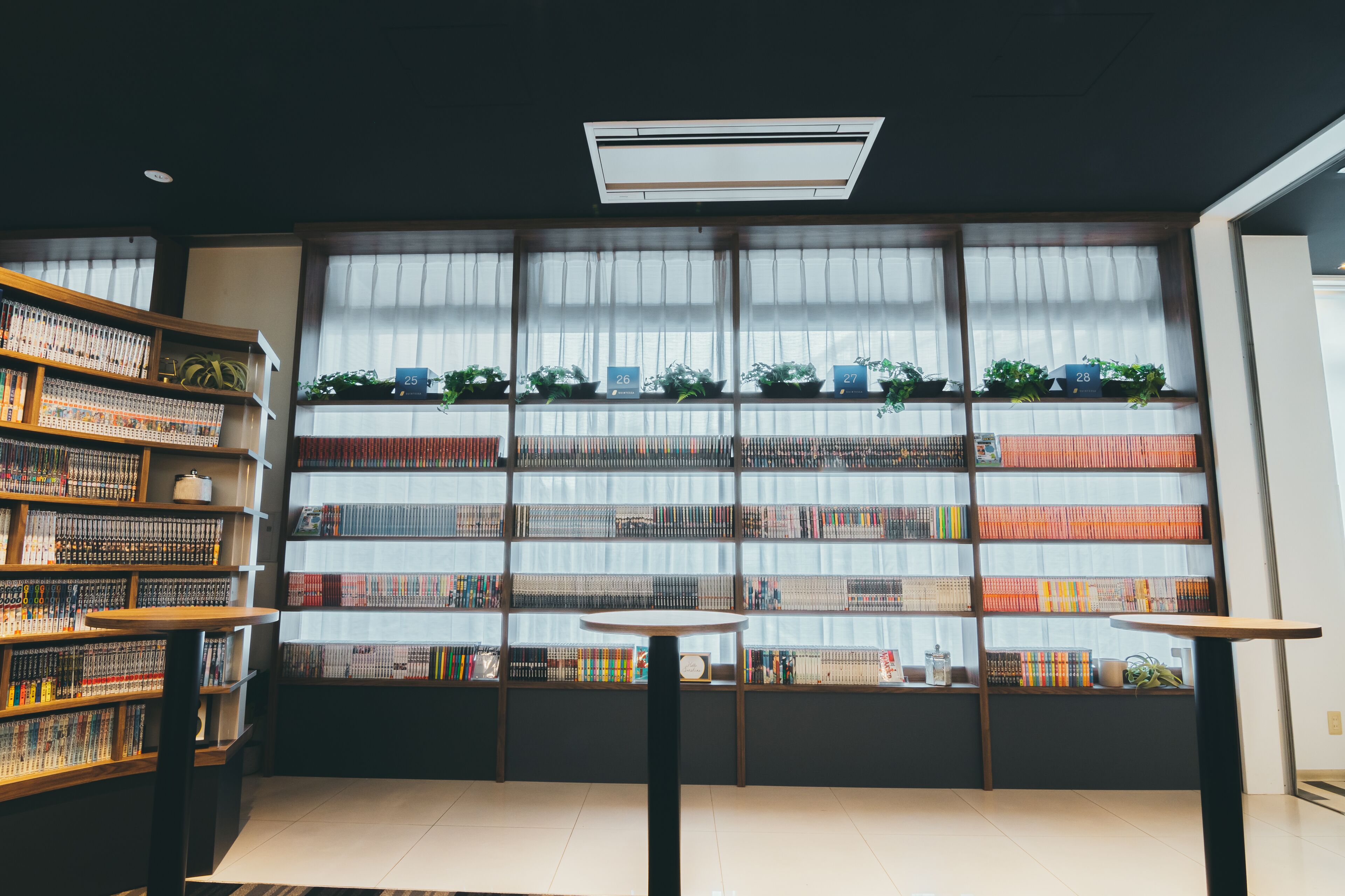 A library with bookshelves, a table, and a window with plants.