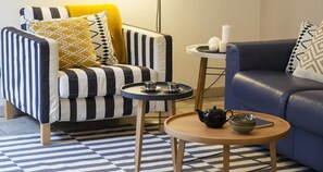 A modern living room with a striped sofa, a blue sofa, a small round wooden table with a teapot and cups, and a side table with candles. - Charming Modern Apartment (Como)