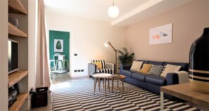 A modern living room with a blue sofa, striped armchairs, a round coffee table, and a patterned rug. - Charming Modern Apartment (Como)