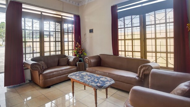 A living room with a brown leather sofa, a matching ottoman, and large windows with red curtains. - Hotel O Borneo (Tondano)