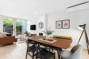 Un salon moderne comprenant un coin repas, un téléviseur à écran plat fixé au mur et une grande fenêtre offrant une vue sur l’extérieur.